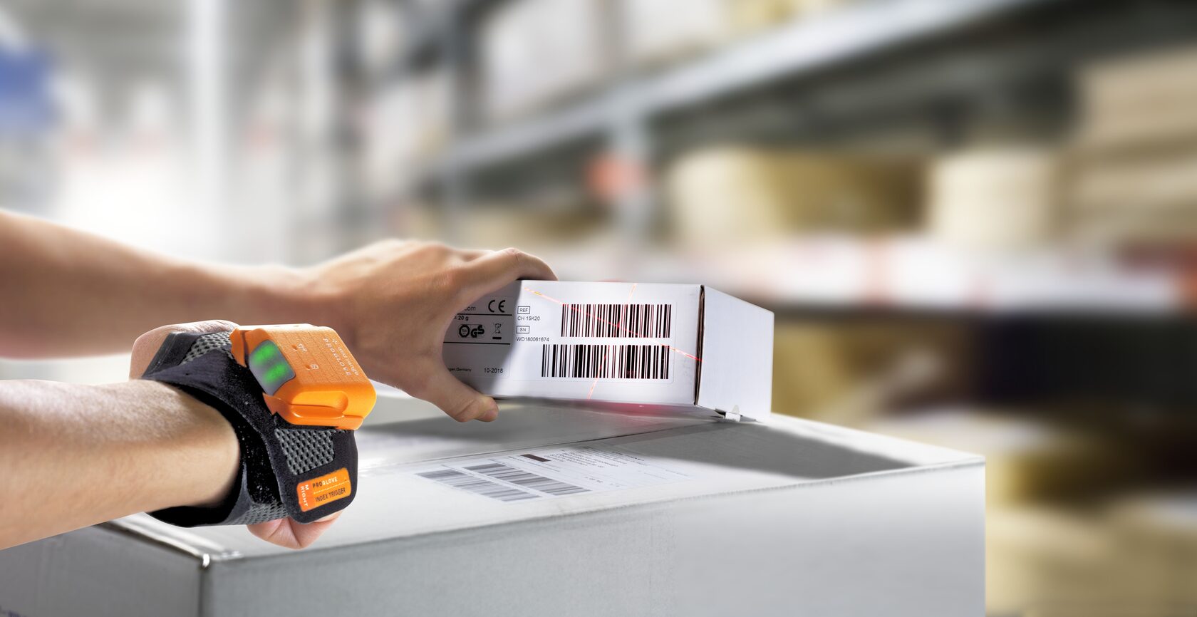 a hand with a ProGlove index trigger wrap and Mark 2 scanner, scanning a barcode on a box